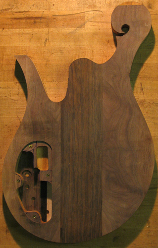 A bass guitar body from the back right after cutting out the body shape with scroll, black walnut top wood and control cavity