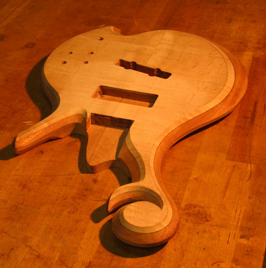 Carved scroll and arm bevel on a custom bass with flamed maple top